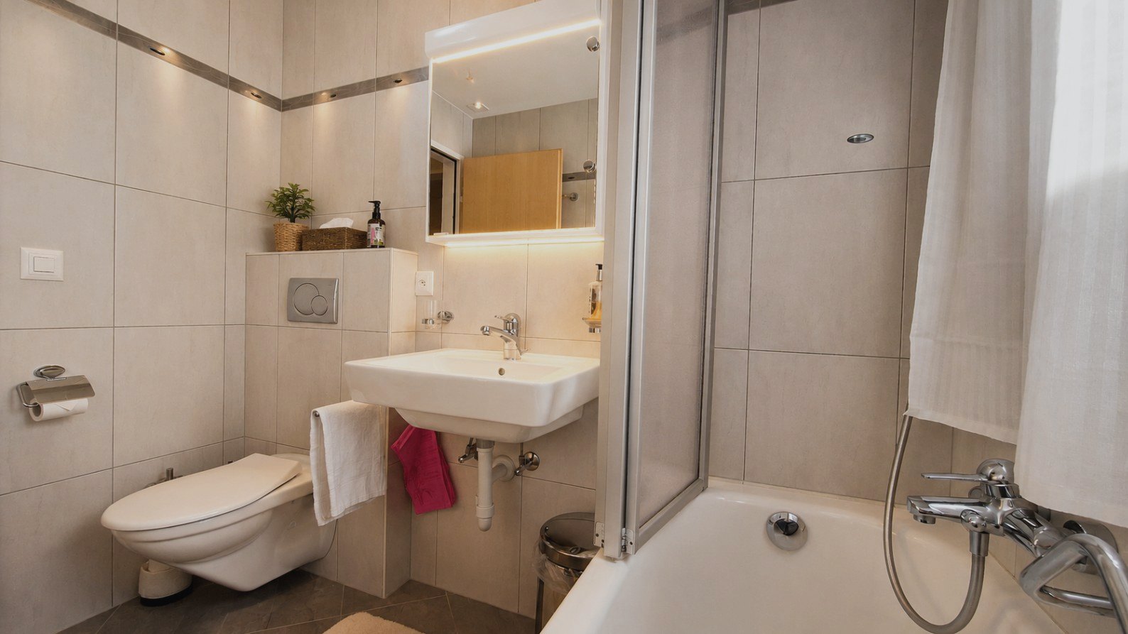 Salle de bain lumineuse d'Auri avec baignoire, douche et miroir éclairé