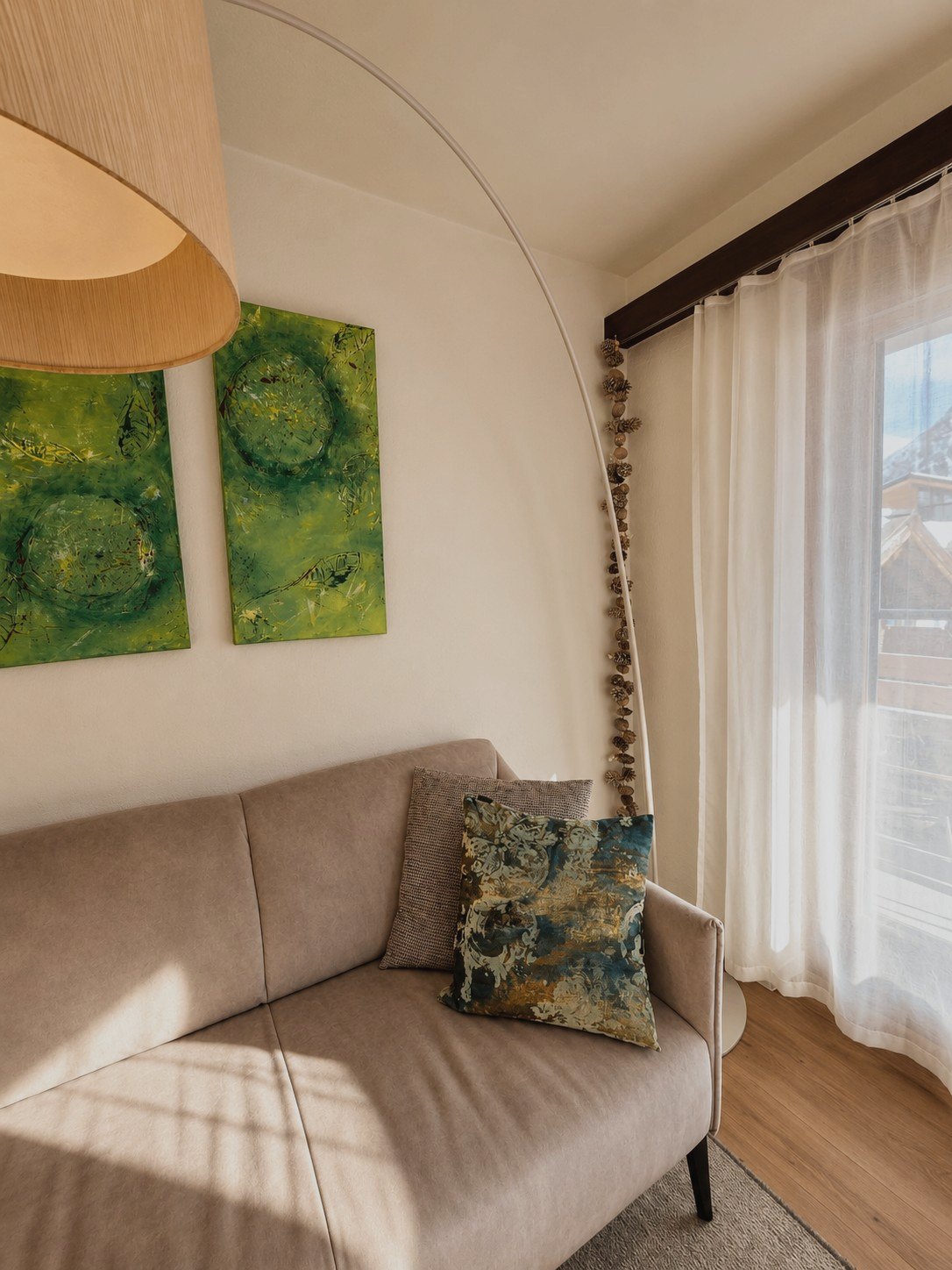 Détail du séjour d'Auri : canapé avec coussins, œuvre verte et lampe arc près de la fenêtre