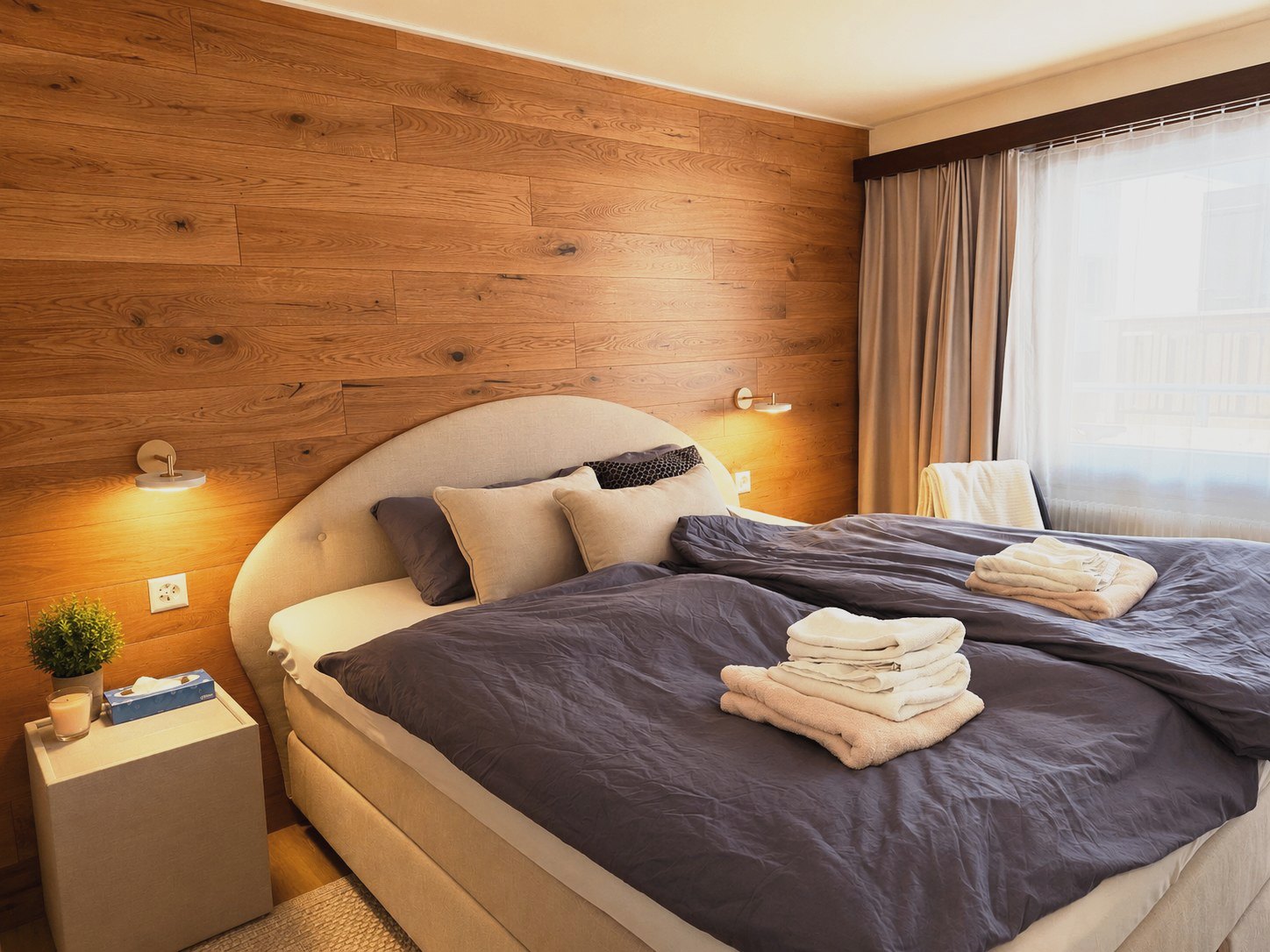 Chambre d'Auri avec paroi en planches de bois, lit boxspring et appliques murales