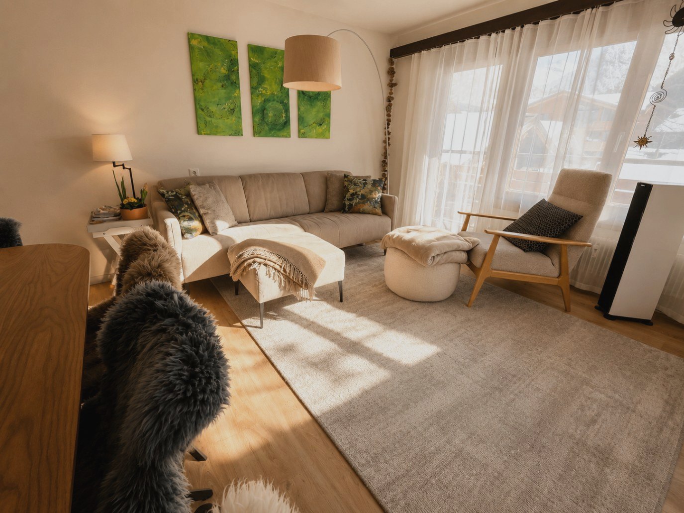 Séjour d'Auri à Saas-Fee avec canapé clair, fauteuil à oreilles, lampe arc et œuvre verte