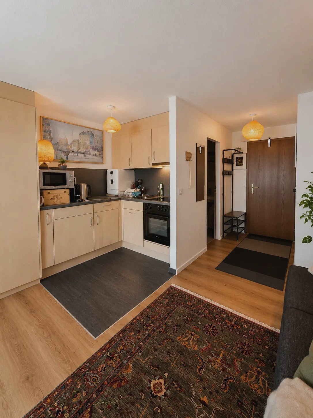 Open kitchen of the Malo studio with light cabinets, microwave and view to the entrance