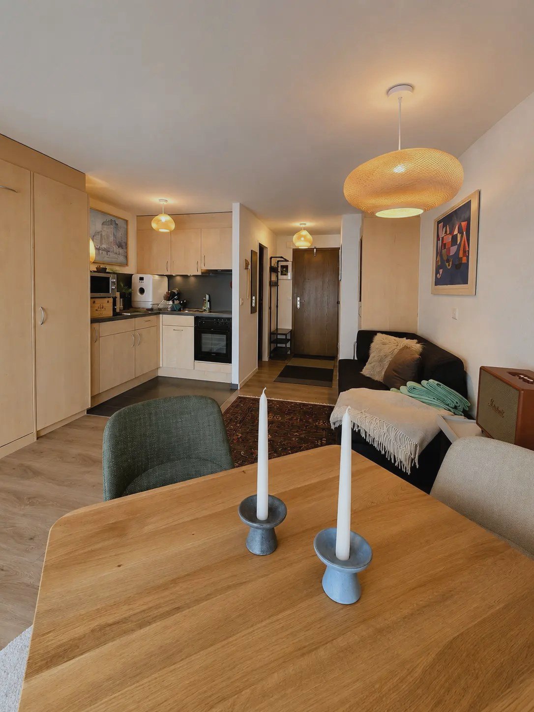 Living and dining area of the Malo studio in Saas-Fee with wooden table, sofa and open kitchen