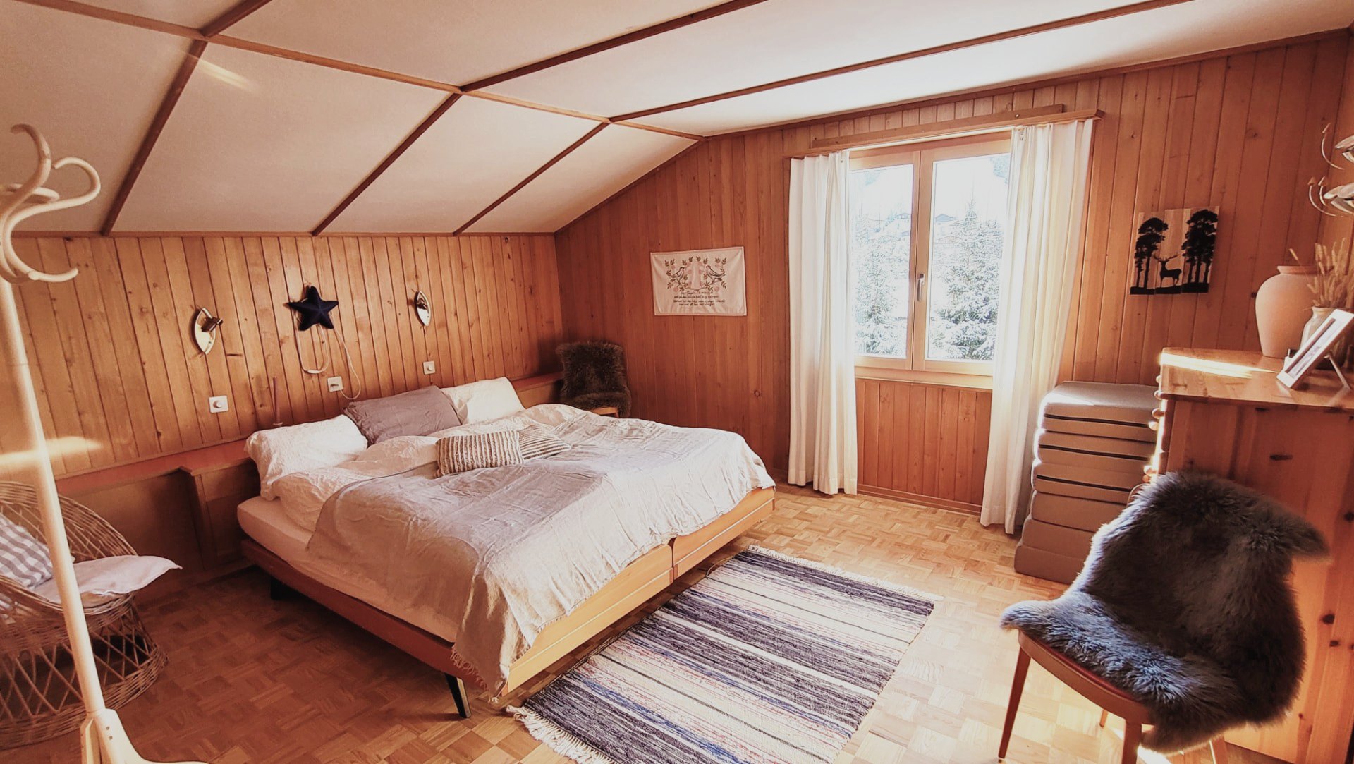 Schlafzimmer im Chalet Nördli mit Holzvertäfelung, Doppelbett und Blick auf verschneite Tannen