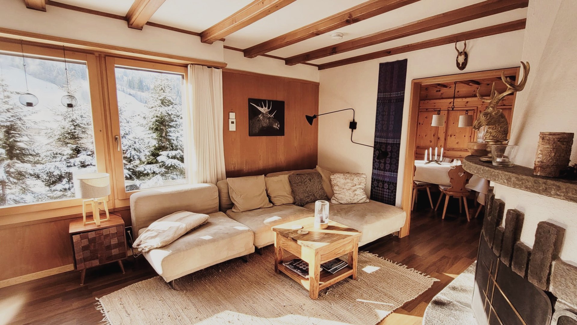 Wohnraum im Chalet Nördli mit Sofa, Holzbalken und grossem Fenster auf die Winterlandschaft