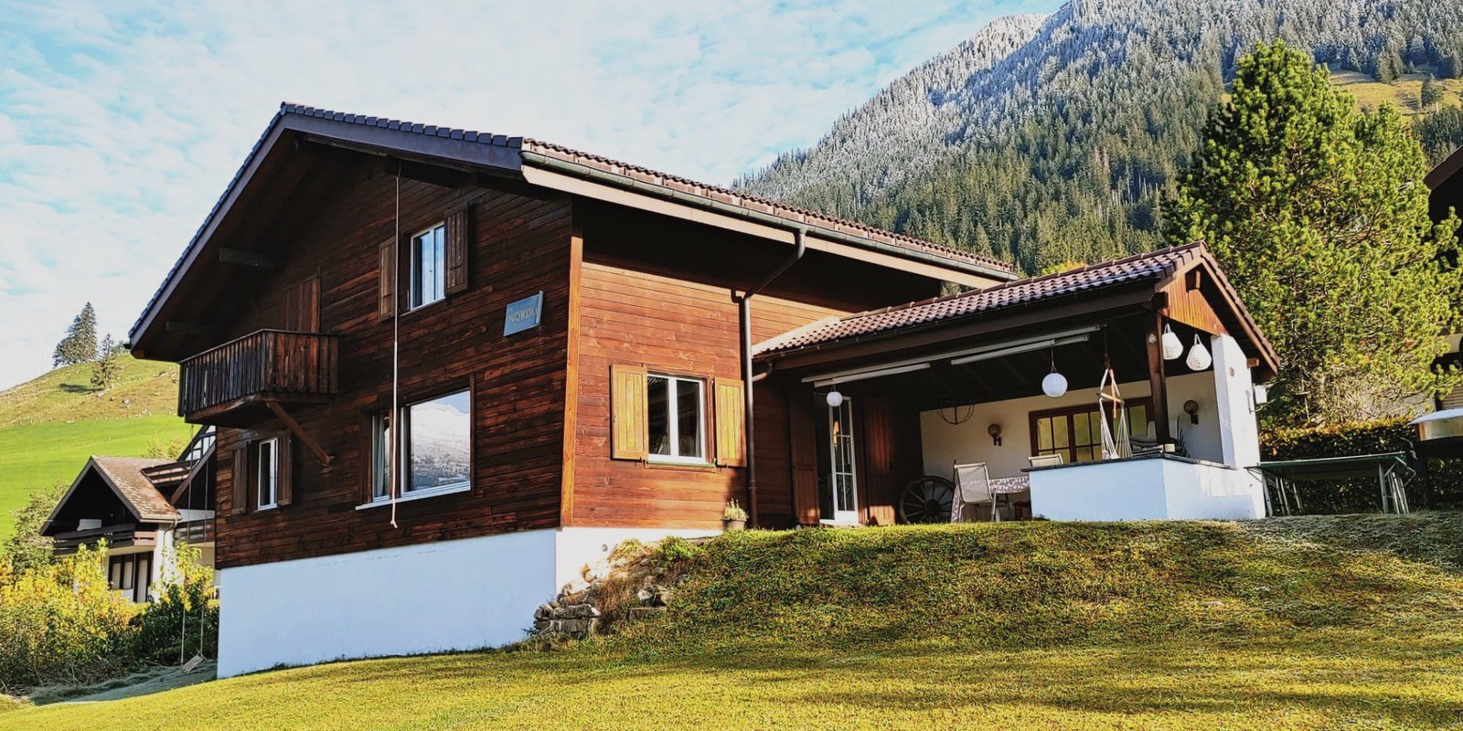 Chalet Nördli in Sörenberg: Holzfassade mit Balkon und überdachter Terrasse vor bewaldetem Berghang