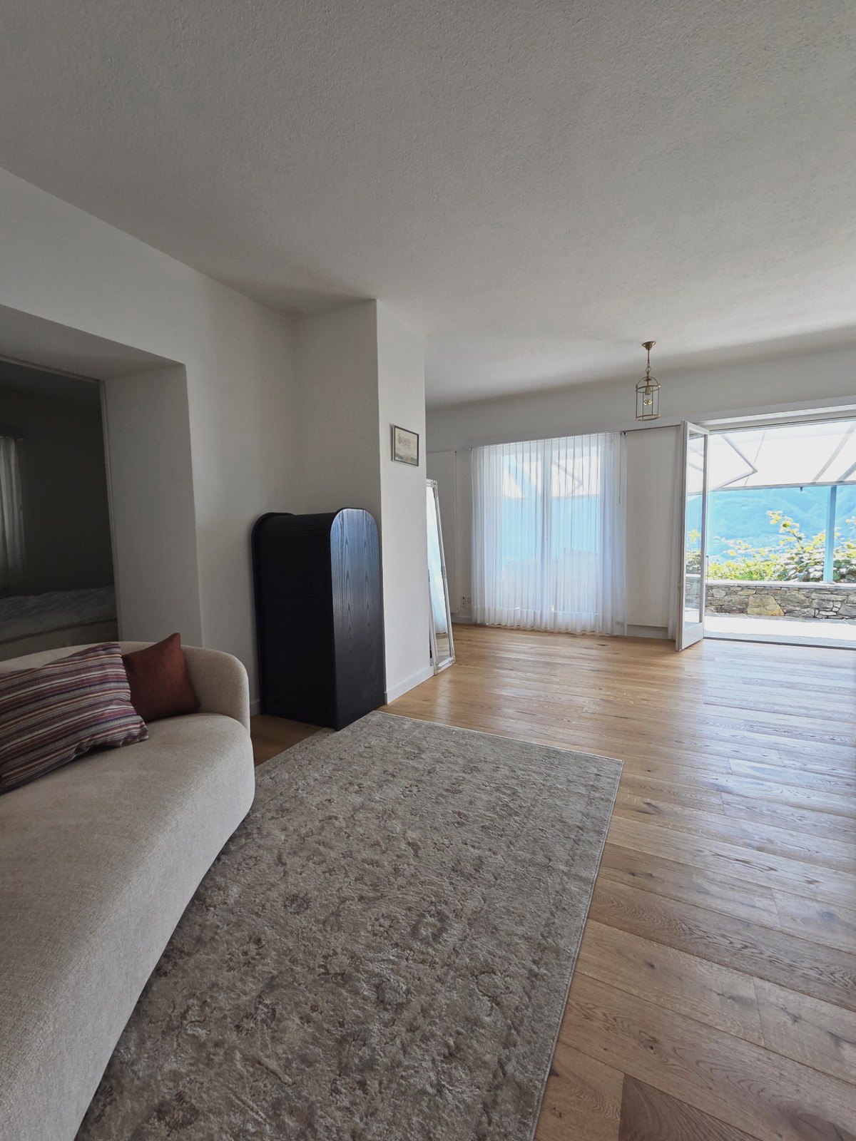 Wohnraum von Soleo mit Eichenparkett, hellem Sofa und geöffneter Tür zur Terrasse